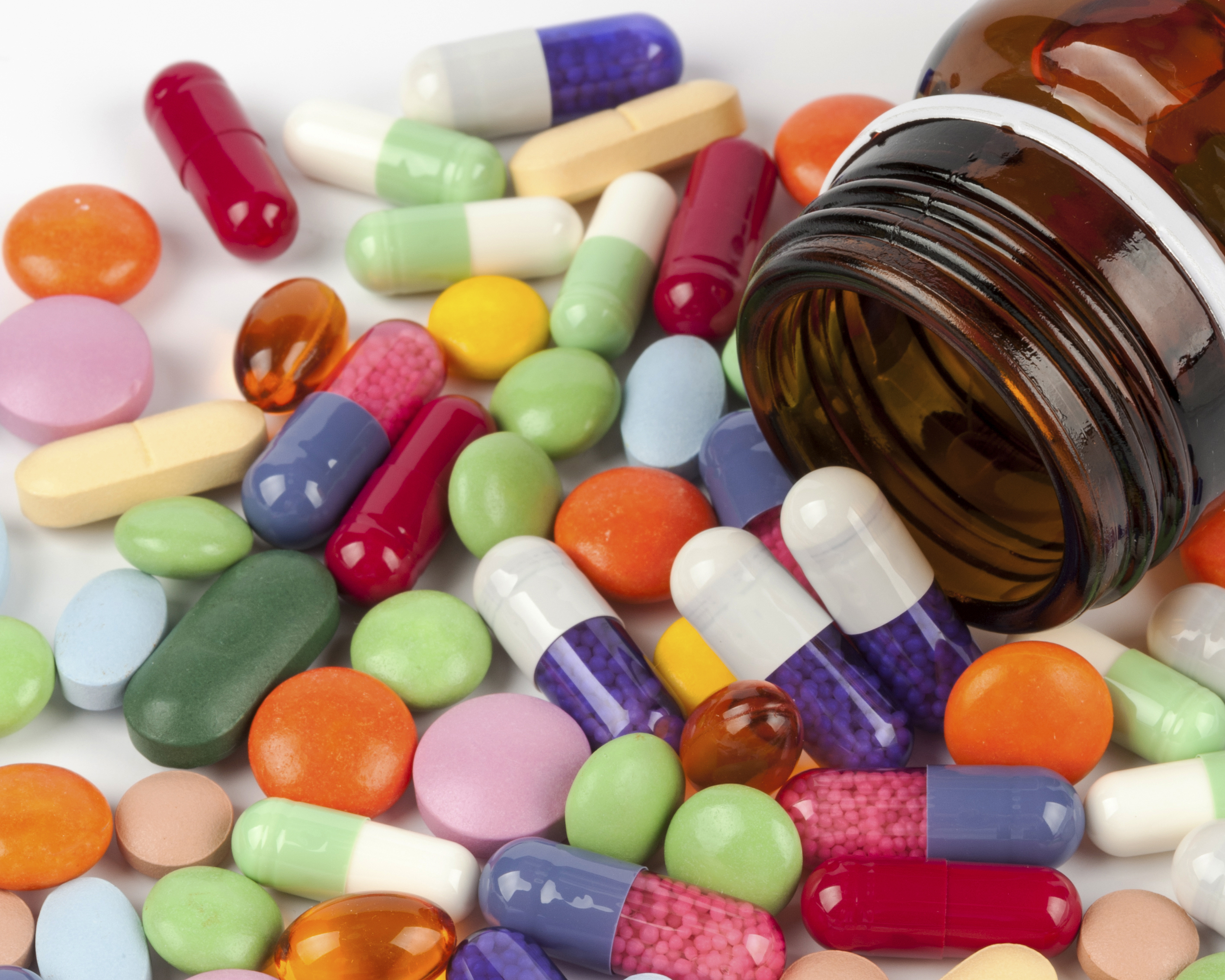 A tipped jar surrounded by colorful pills and caplets.