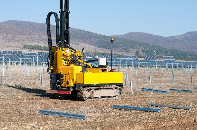 solar panel field being installed. tractor equipment pounding posts into the ground. posts hold the solar panels up.